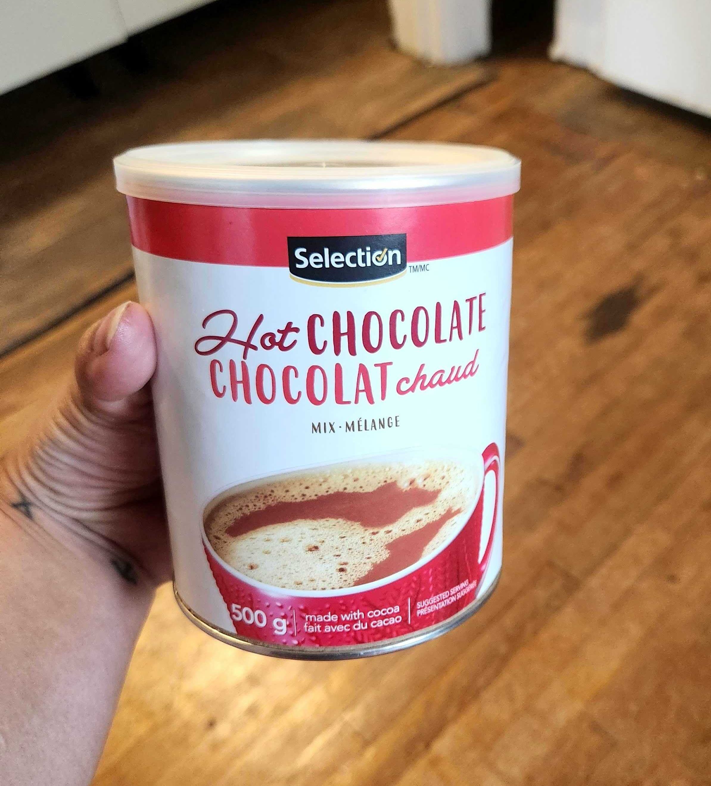\u200bSarah holding a tin of Selection brand hot chocolate mix from Metro, $4.49 for 500 grams.