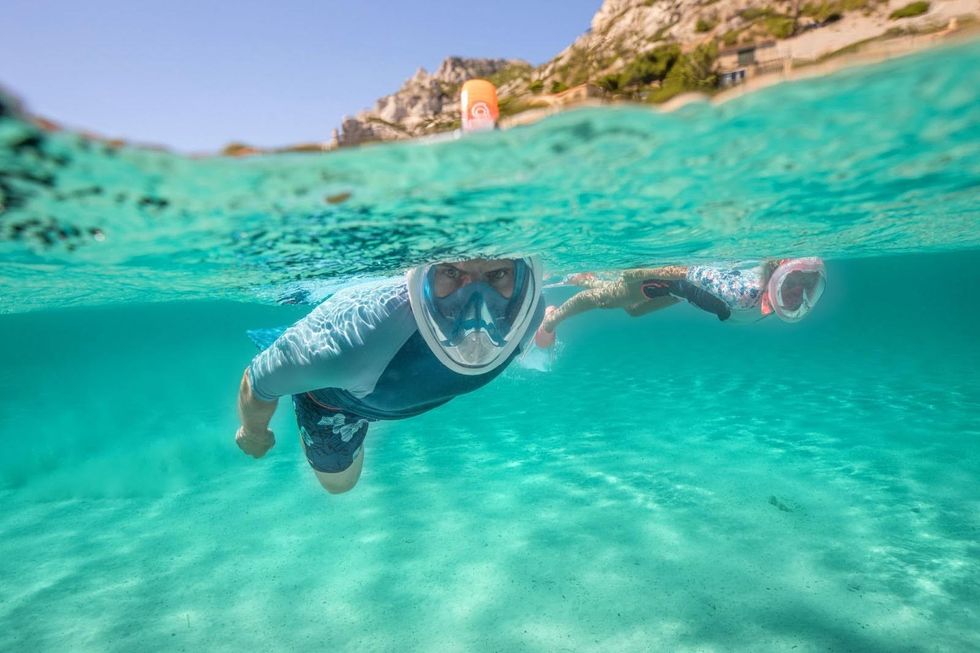 \u200bTwo people swim wearing full-face snorkel masks.