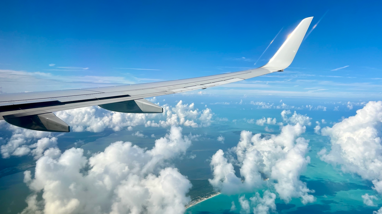 Un aileron d'avion surplombe des nuages et une mer turquoise.