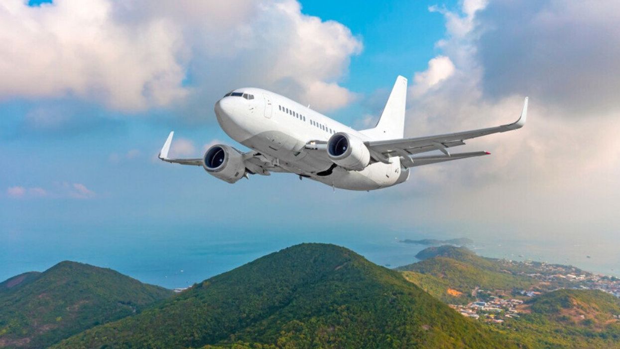 Un avion survolant l'océan et les montagnes d'une île tropicale.