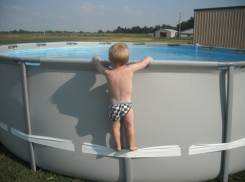 Un b\u00e9b\u00e9 grimpe sur le bord d'une piscine. 