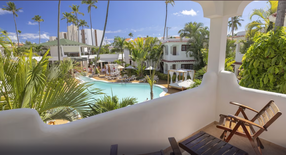 Un balcon d'h\u00f4tel donne vue sur une piscine et des palmiers.