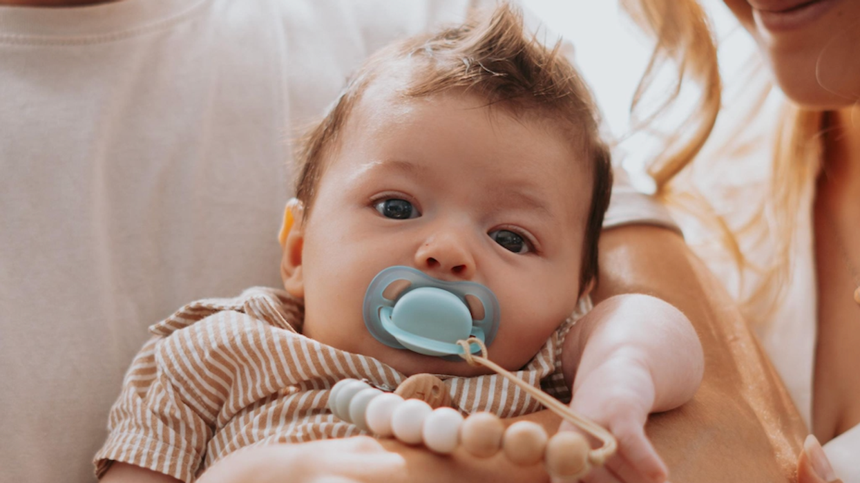 Un bébé avec sa suce dans les bras de ses parents.