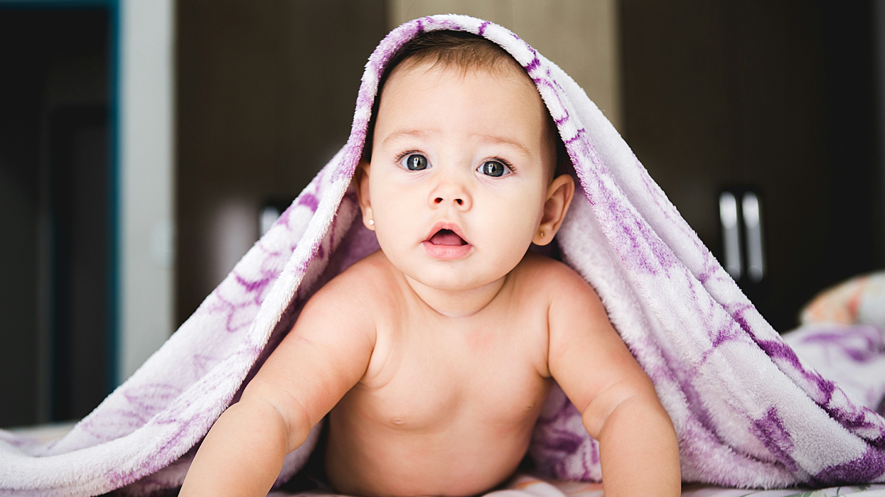 Un bébé couché sur le ventre sous une couverture mauve.