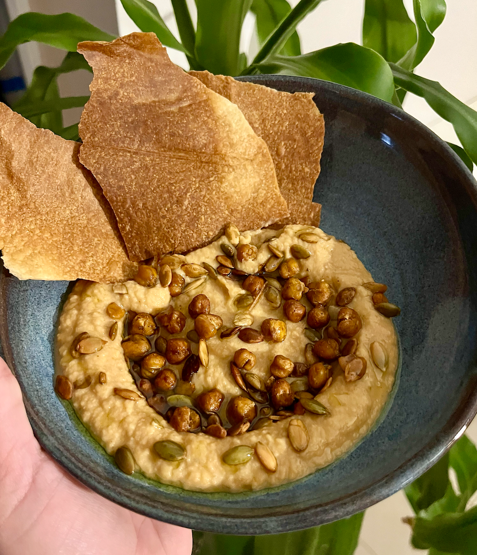 Un bol de houmous avec des pois chiches r\u00f4tis et des graines de citrouille r\u00f4ties en garniture.