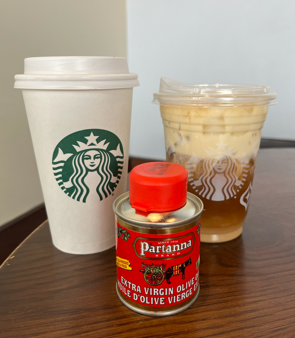 Un caf\u00e9 Starbucks dans un verre en carton, un caf\u00e9 glac\u00e9 dans un verre transparent, et un pot d'huile d'olive.