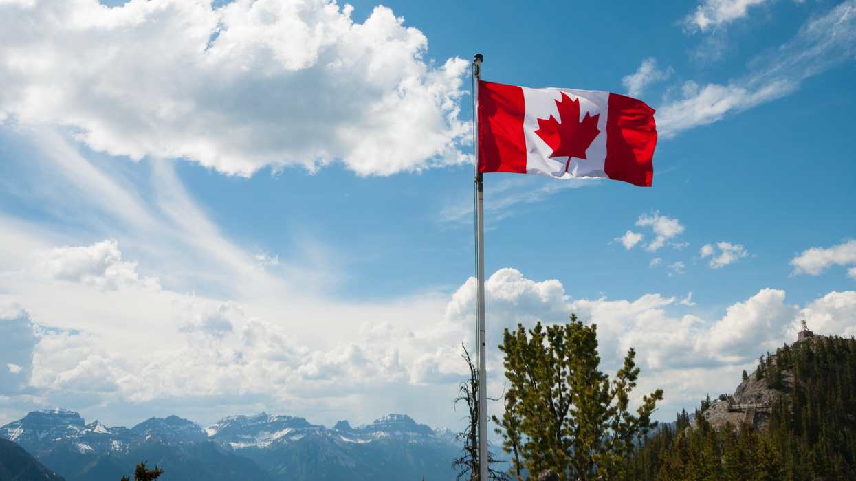 Un drapeau du Canada dans un paysage où l'on voit des rocheuses au loin.
