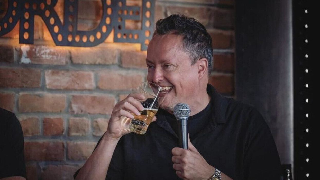 Un homme rit et s'apprête à prendre une gorgée de sa bière avec un micro dans l'autre main.