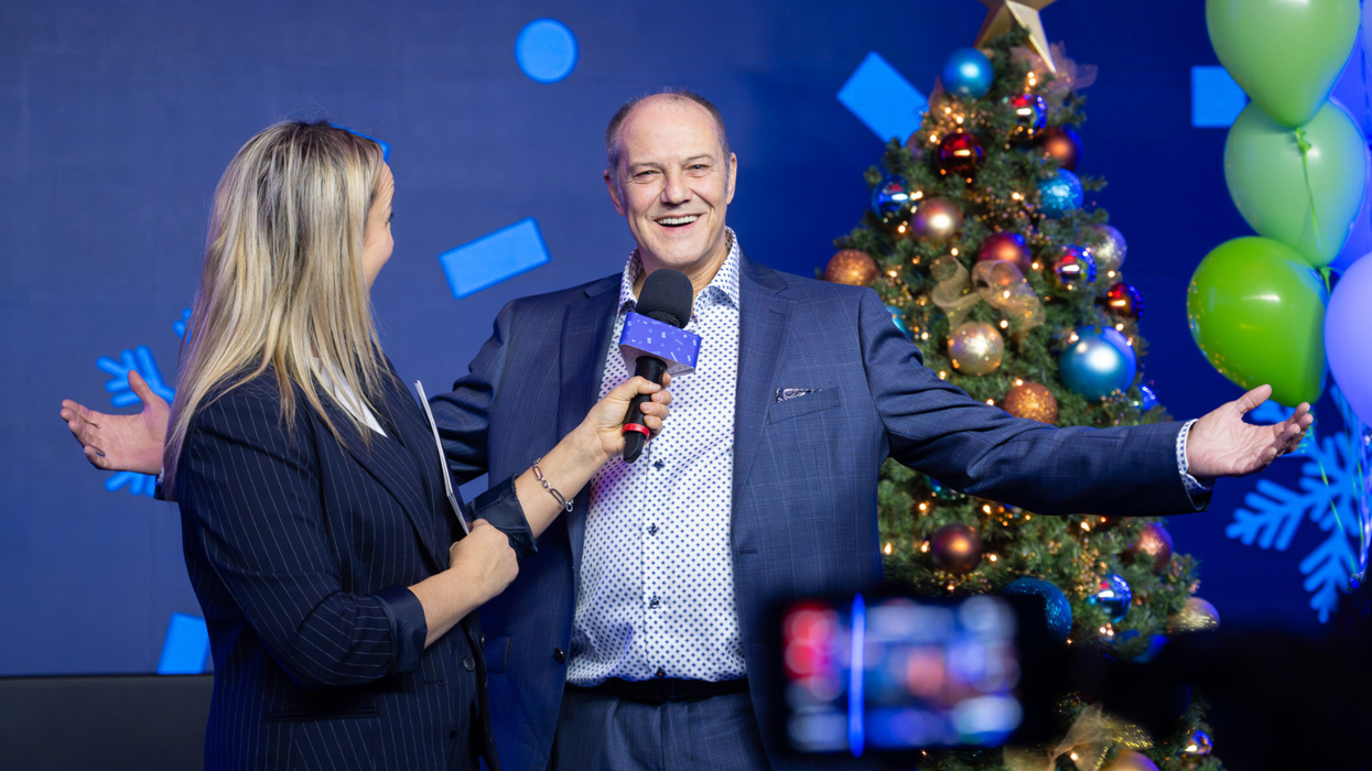 Un homme sourit avec les bras ouvert devant une dame qui lui tend le micro.