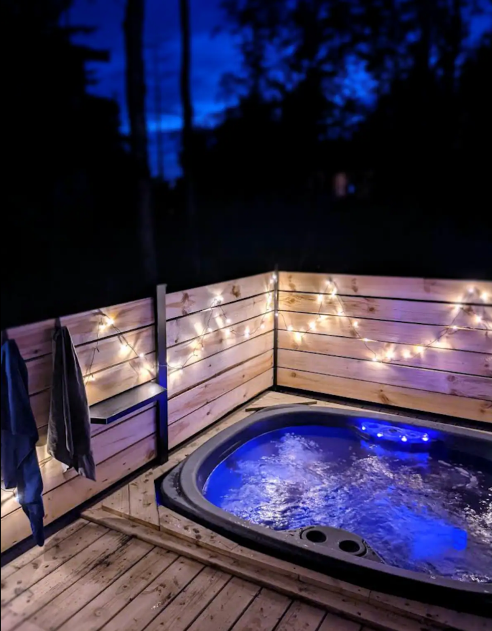 un jacuzzi int\u00e9gr\u00e9 \u00e0 une terrasse en bois, illumin\u00e9e par des guirlande durant la nuit