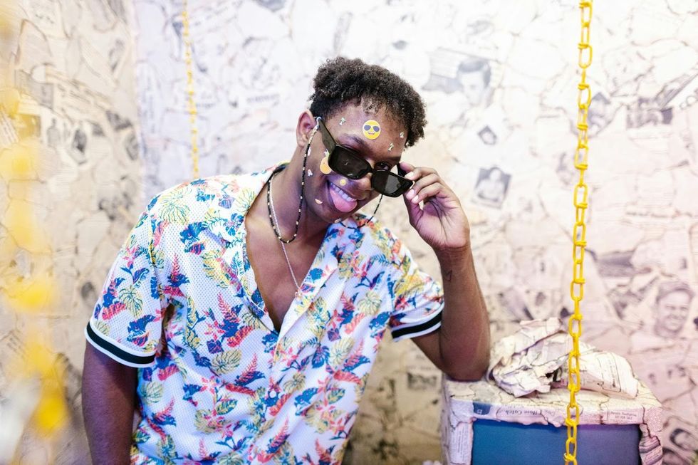 Un jeune homme portant une chemise hawa\u00efenne, des lunettes de soleil avec une cha\u00eene et des autocollants sur le visage.