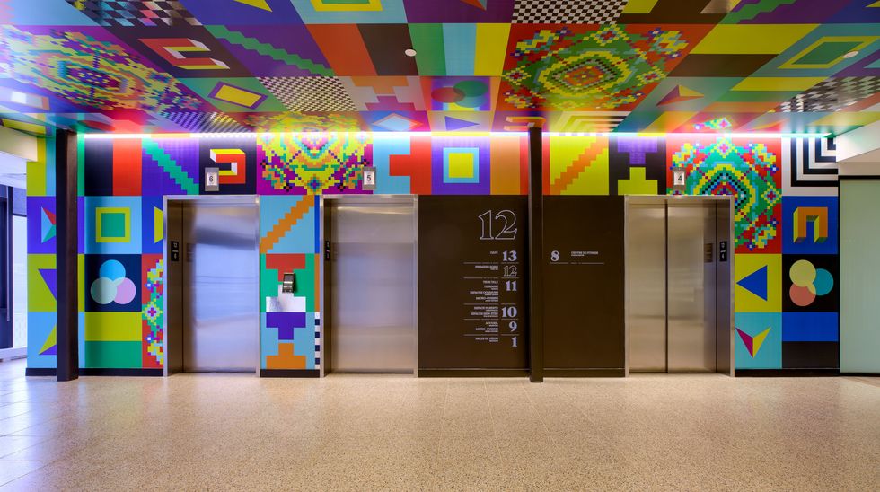 Un mur rempli d'oeuvres d'art color\u00e9es autour de portes d'ascenceur.