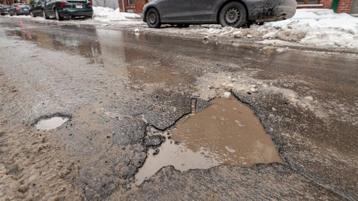 Un nid-de-poule au milieu d'une route et des voitures sont stationnées sur le côté de la rue.