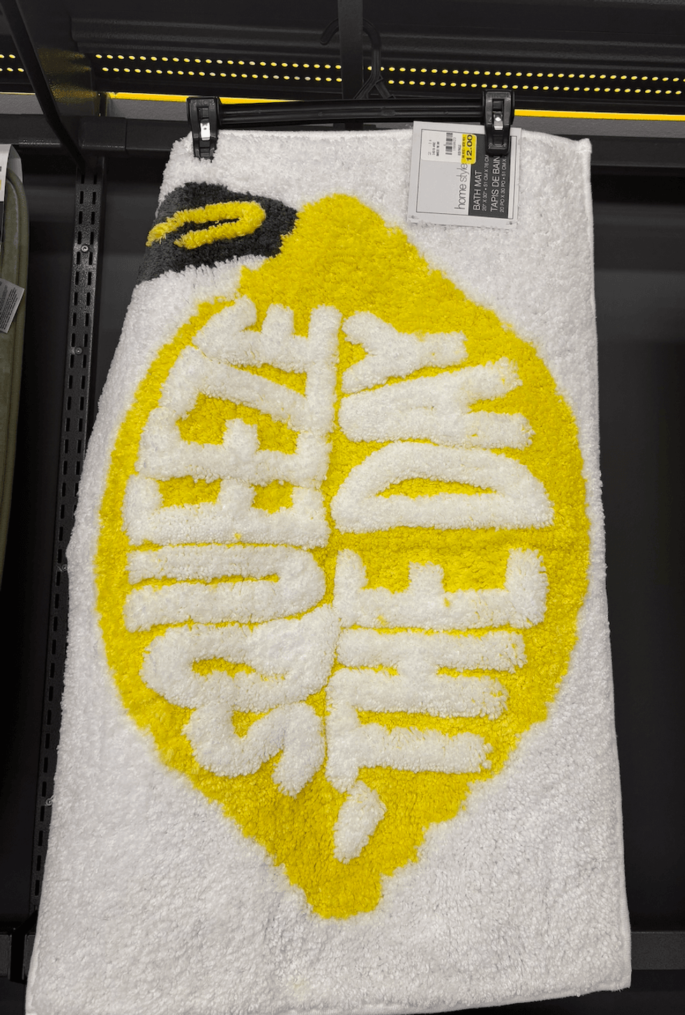 Un tapis de bain blanc avec une forme de citron jaune portant l'inscription \u00ab Squeeze the Day \u00bb.