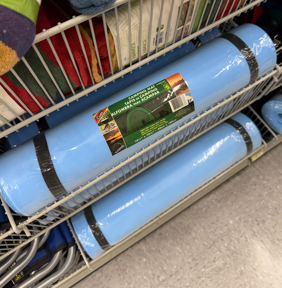 Un tapis de sol bleu enroul\u00e9, attach\u00e9 avec deux sangles noires et rang\u00e9 dans un panier m\u00e9tallique.