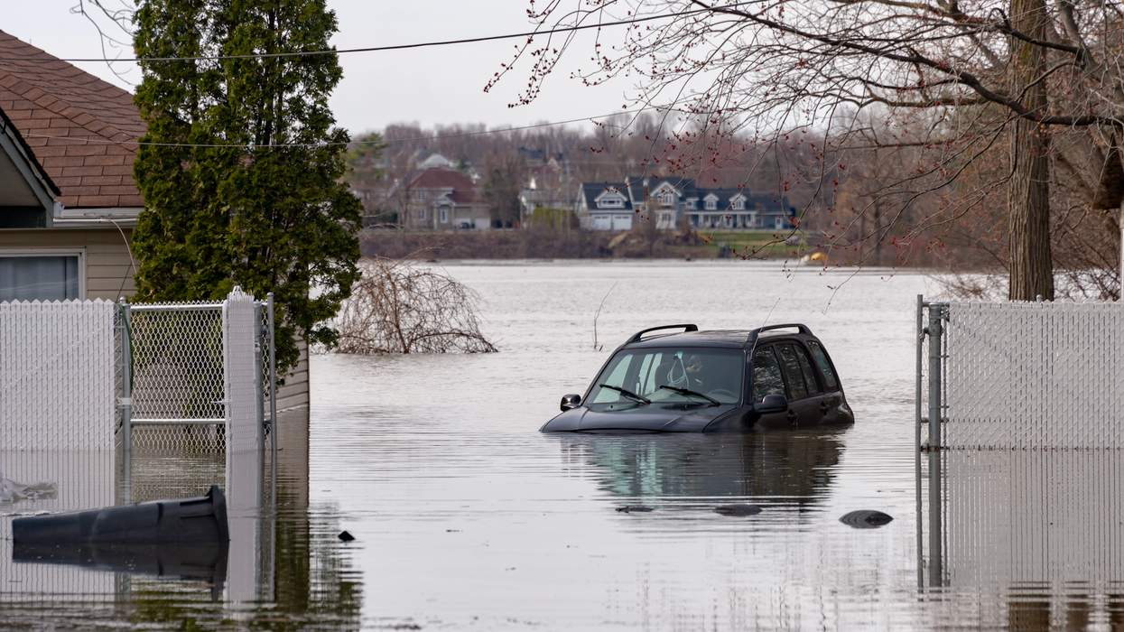 Un véhicule est dans un terrain inondé près d'un lac et d'une maison.