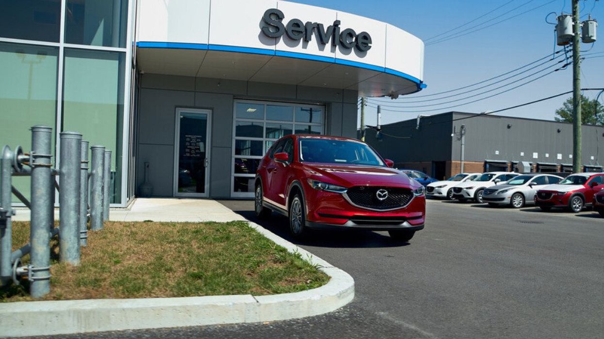 Un véhicule rouge foncé de la marque Mazda est placé devant un édifice où il est inscrit « Service ».