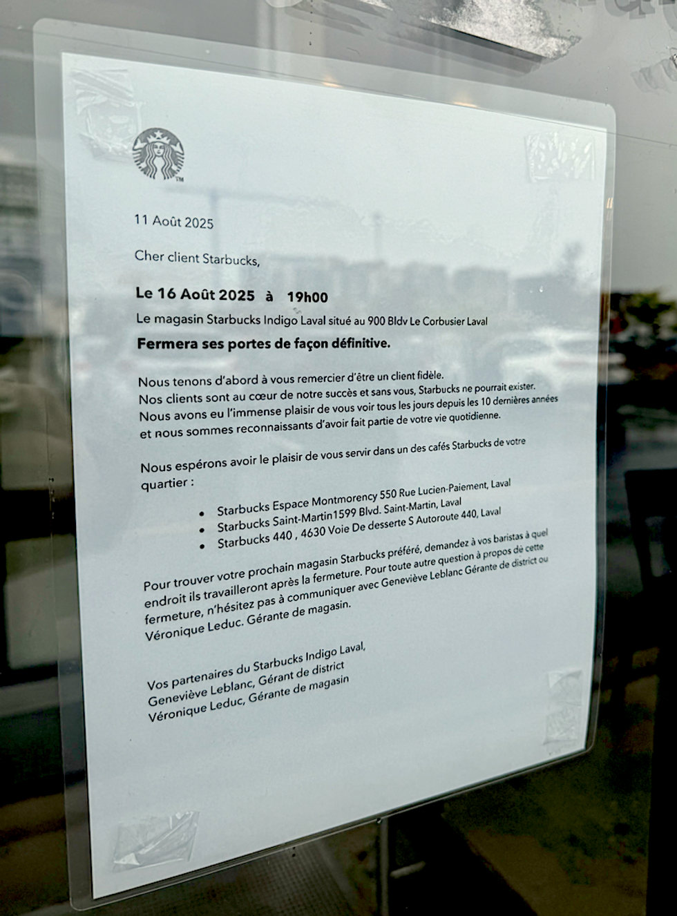 Une affiche dans la fen\u00eatre de la porte d'entr\u00e9e au Starbucks du Quartier Laval, \u00e0 c\u00f4t\u00e9 du Indigo.