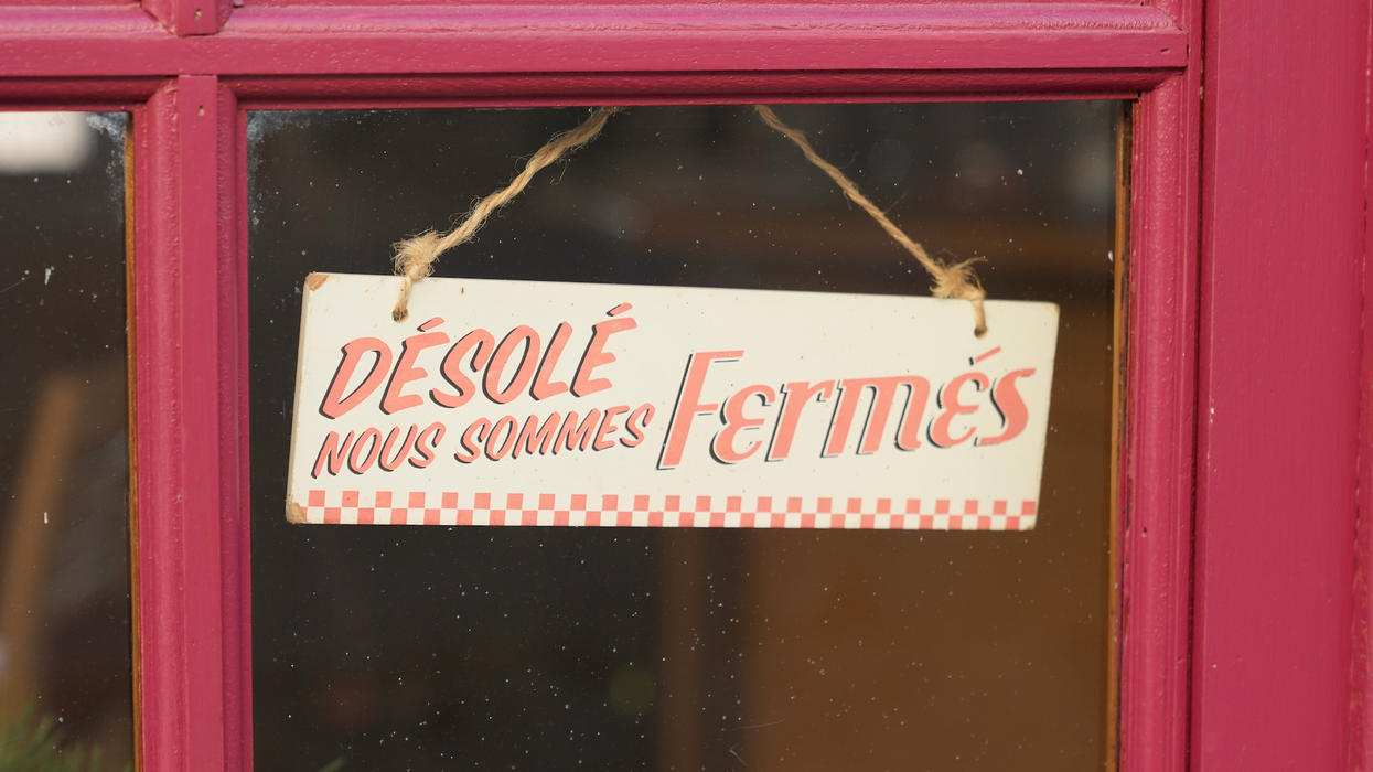Une affiche « Désolé nous sommes fermés » est placé dans la fenêtre d'une porte rouge.