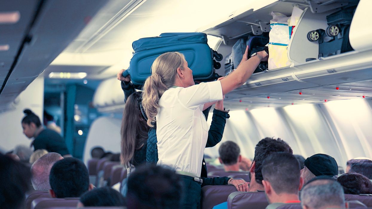 Une agente de bord aide les passagers et passagères à placer leurs bagages dans la cabine d'un avion.
