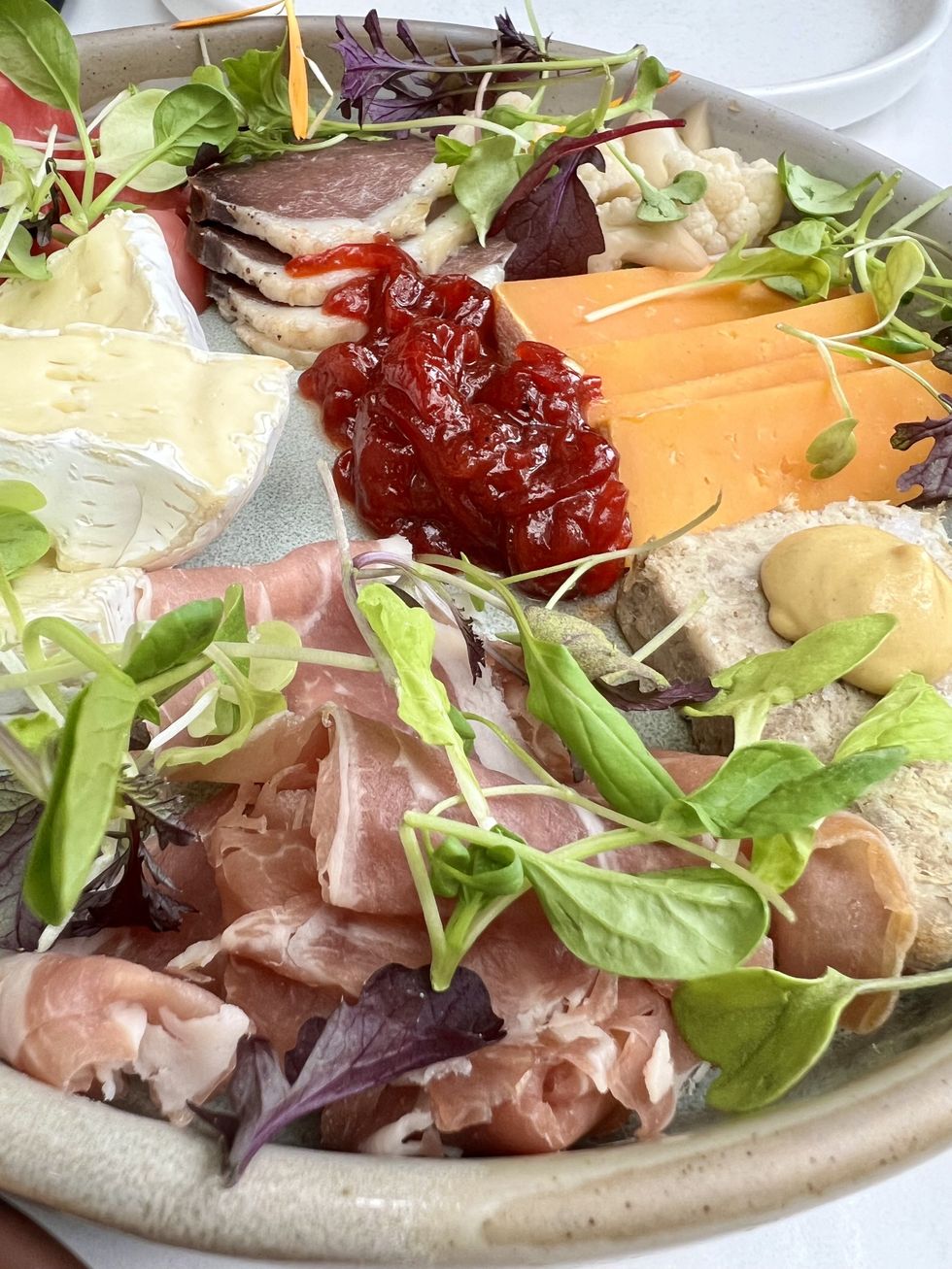 Une assiette de charcuteries et fromages recouverte de basilic.