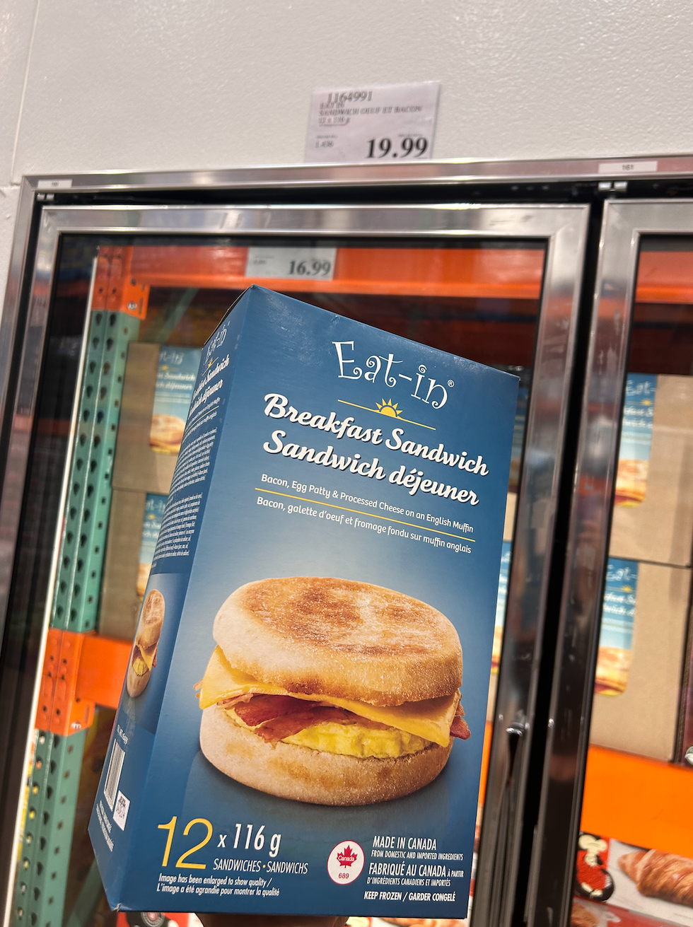 Une boite de sandwich d\u00e9jeuner tenue devant un cong\u00e9lateur du Costco.