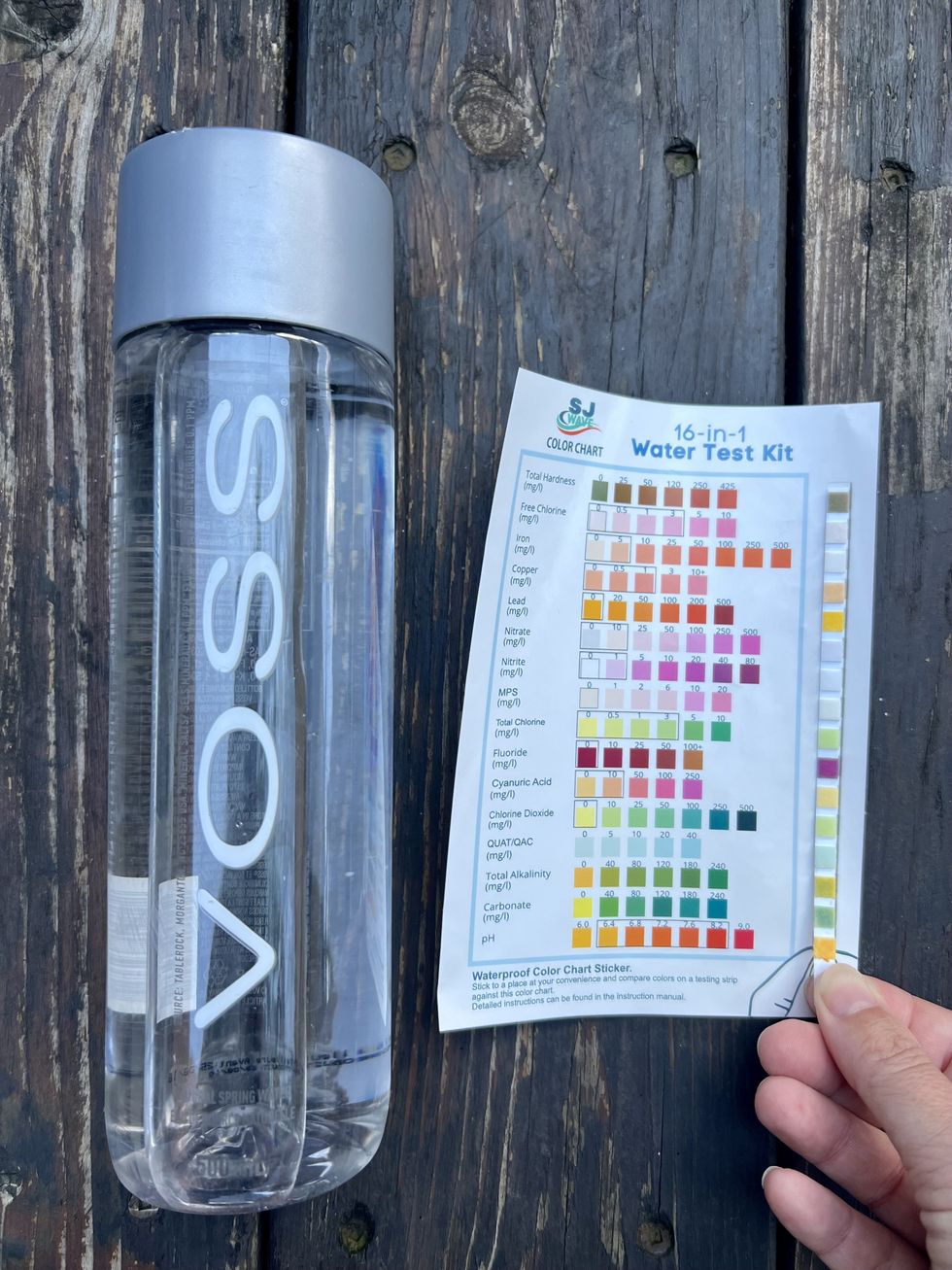 Une bouteille d'eau \u00e0 c\u00f4t\u00e9 d'une charte d'indicateurs et d'une bandelette de test tenue par une main.