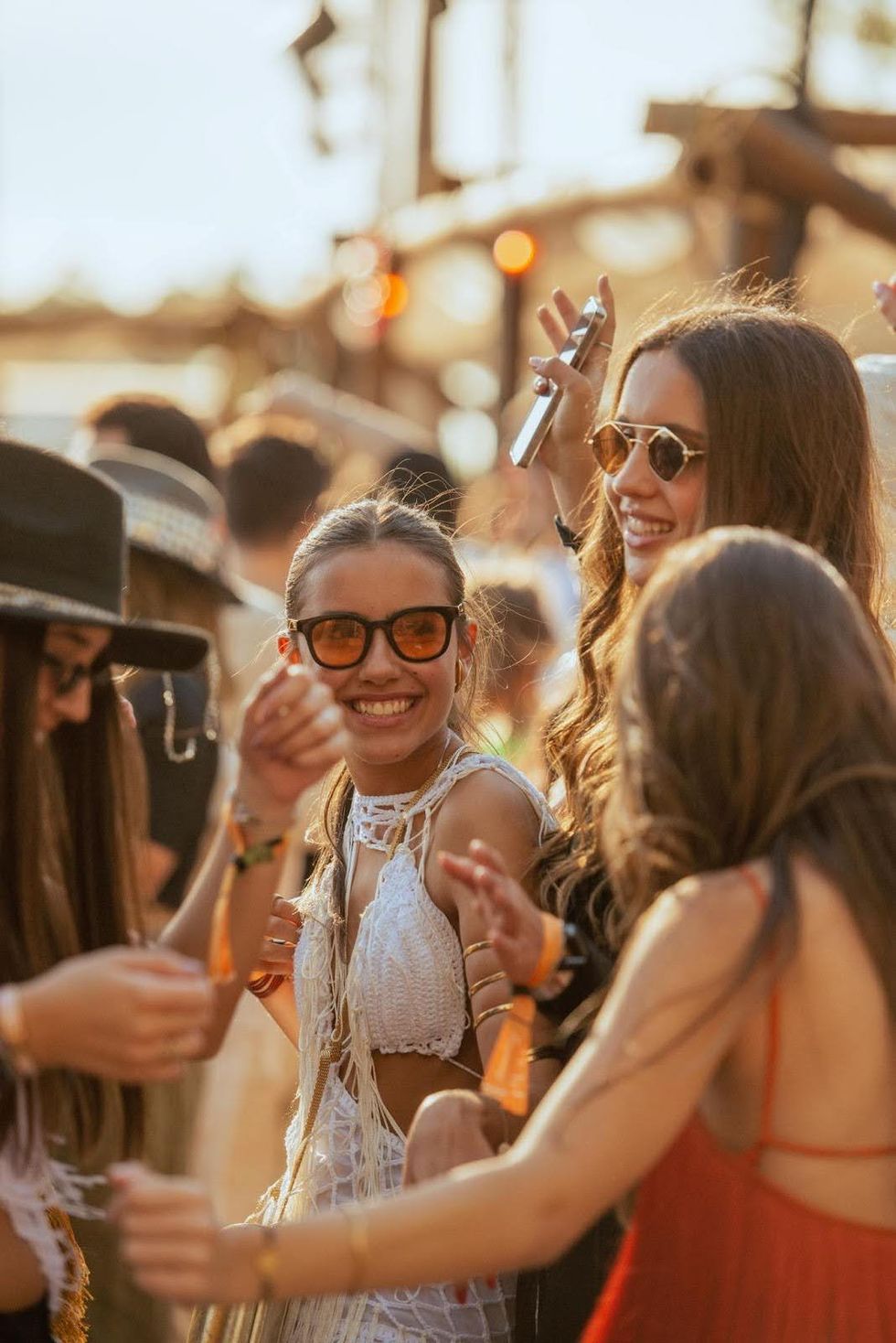 Une femme portant des lunettes de soleil et une robe blanche danse dans la foule lors d'un festival.