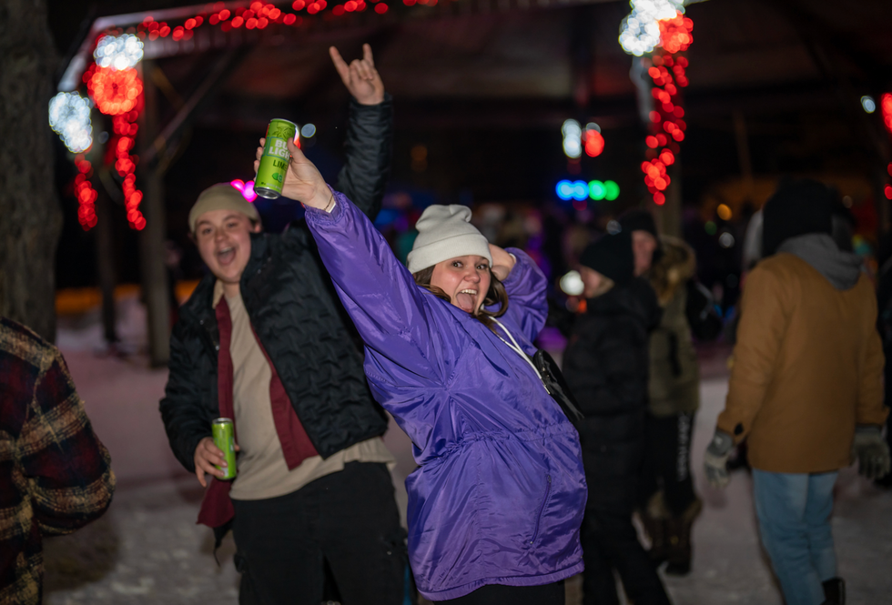 Une femme v\u00eatue d'un manteau d'hiver mauve les bras dans les airs.