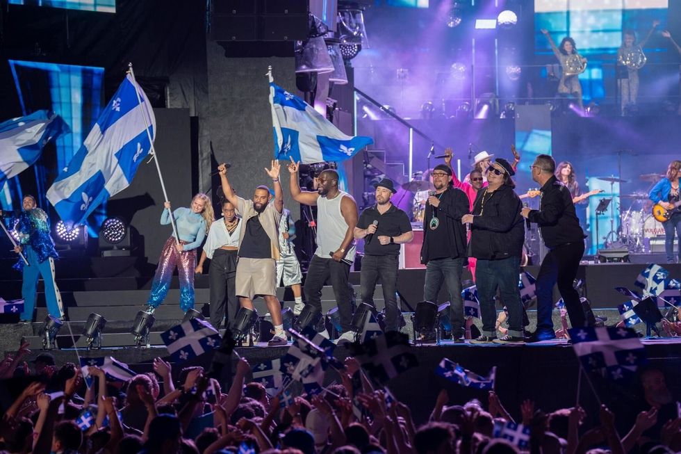 Une foule devant une sc\u00e8ne avec des artistes et des drapeaux du Qu\u00e9bec.