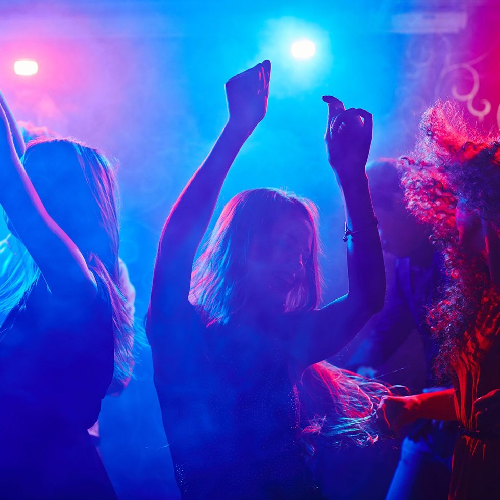 Une jeune fille dansant lors d'une f\u00eate, entour\u00e9e d'une foule anim\u00e9e et \u00e9clair\u00e9e par des lumi\u00e8res n\u00e9on.