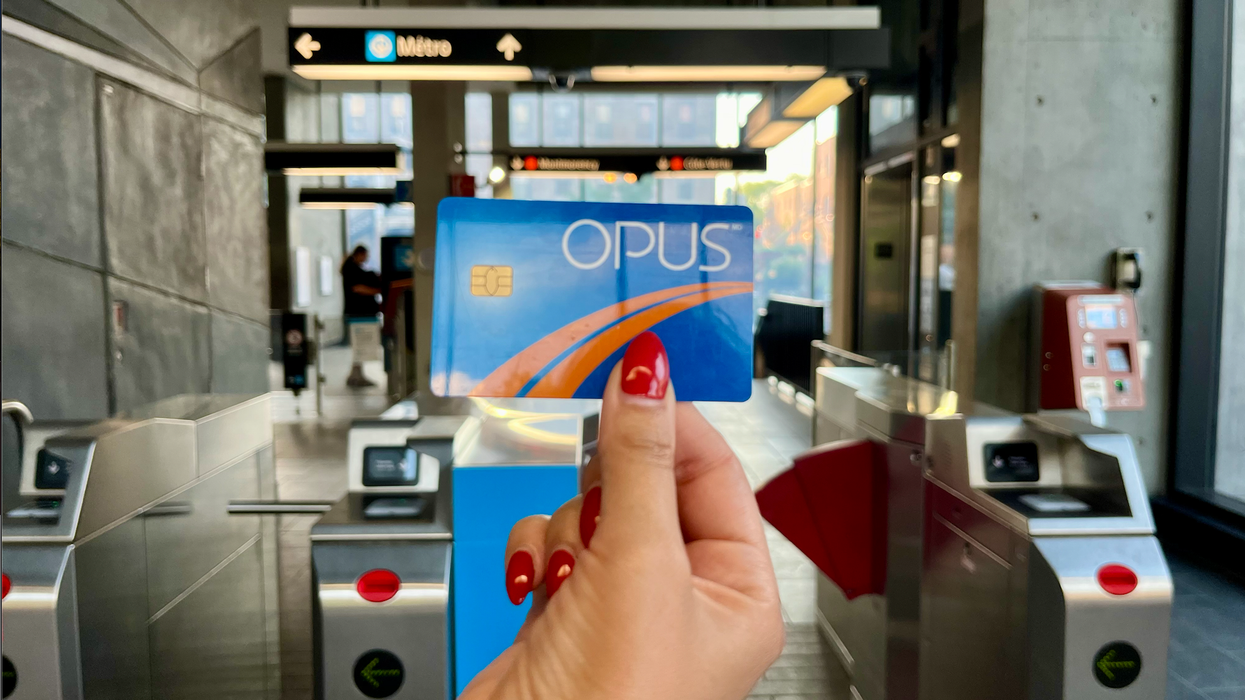 Une main avec des ongles rouges tient une carte OPUS devant les bornes d'accès d'une station de métro.