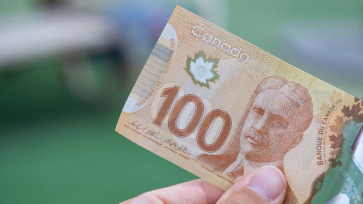 Une main qui tient un billet de 100 $ canadiens.