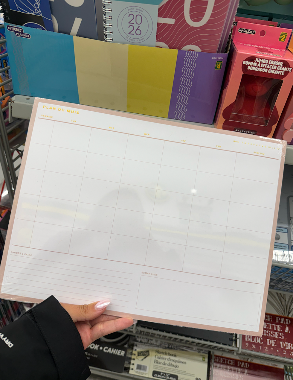 Une main qui tient un planificateur hebdomadaire vendu dans la rang\u00e9e des fournitures scolaires chez Dollarama.
