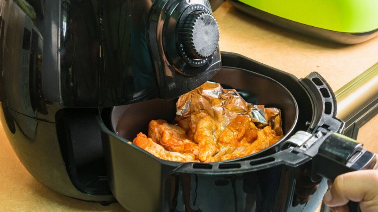 Une main retire le tiroir d'une friteuse à air chaud noire contenant des ailes de poulet.