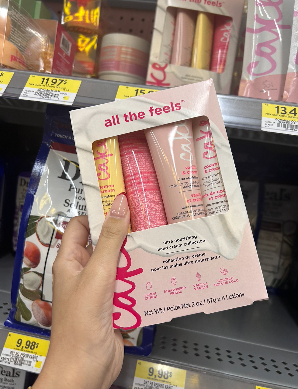 Une main tenant la collection de cr\u00e8mes pour les mains de Cake Beauty devant une \u00e9tag\u00e8re du Walmart.
