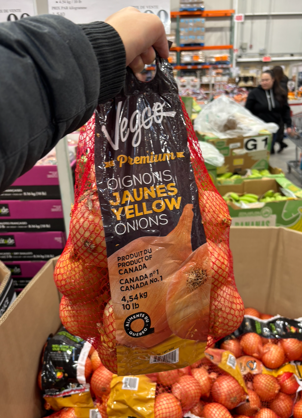 Une main tenant un sac d'oignons jaunes Vegco au Costco.