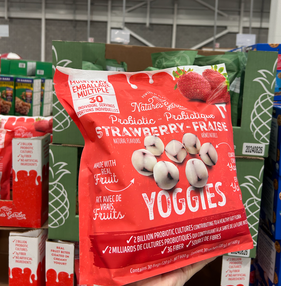 Une main tenant un sac de Yoggies probiotiques \u00e0 la fraise de Nature's Garden devant un \u00e9talage au Costco.