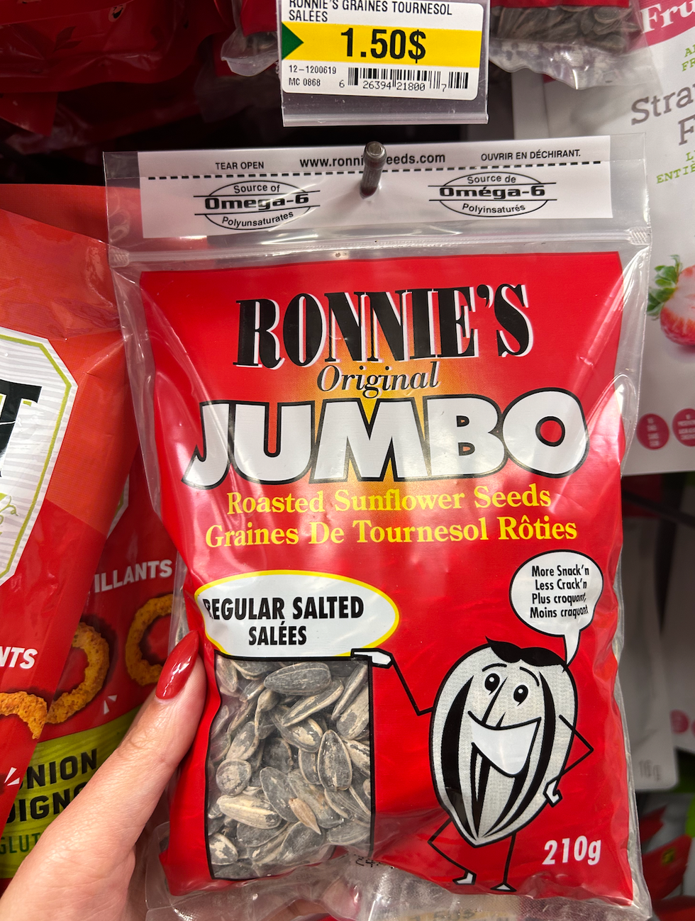 Une main tenant un sac rouge de graines de tournesol au Dollarama.