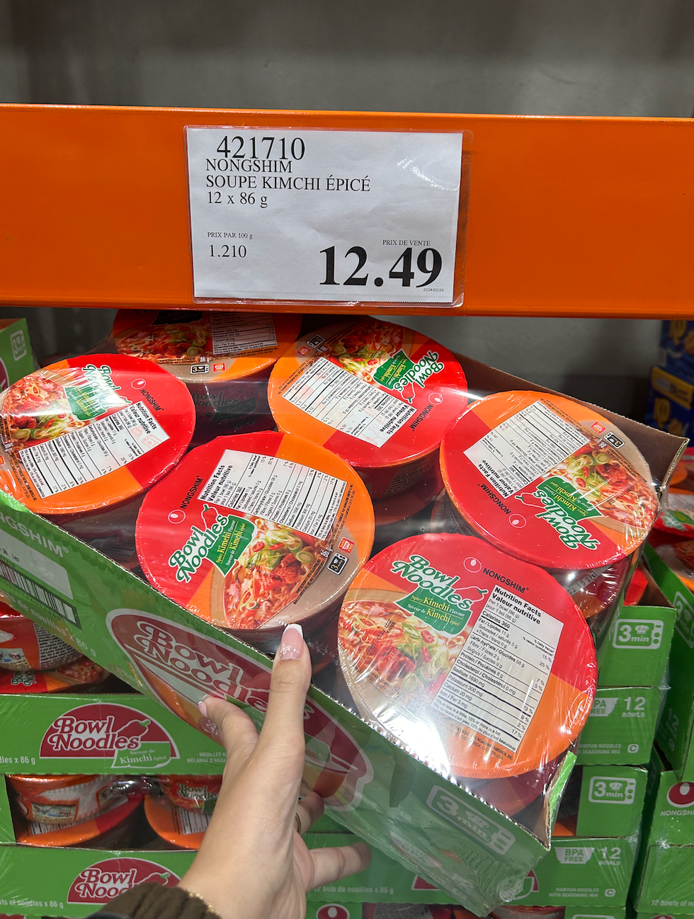 Une main tenant une boite contenant douze soupes au kimchi \u00e9pic\u00e9 devant son \u00e9talage au Costco.