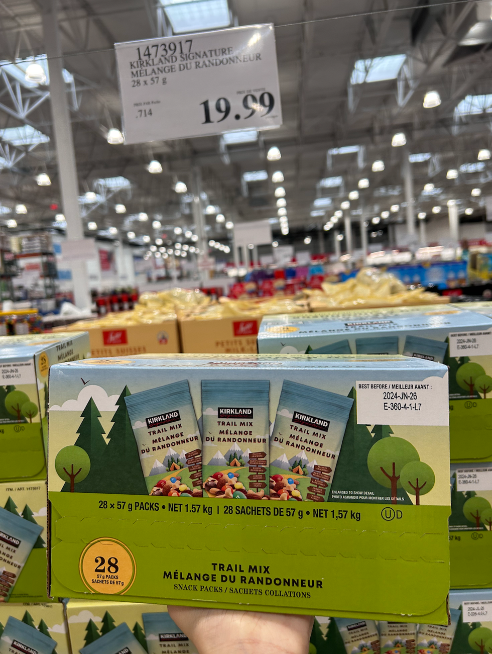 Une main tenant une boite de collations M\u00e9lange du randonneur Kirkland Signature devant un \u00e9talage du Costco.