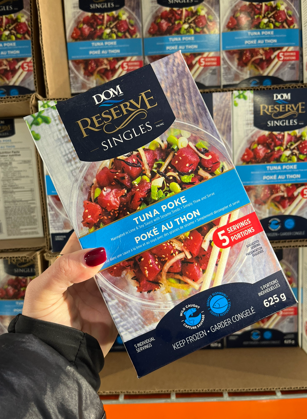 Une main tenant une boite de pok\u00e9 au thon DOM Reserve devant un \u00e9talage du Costco.