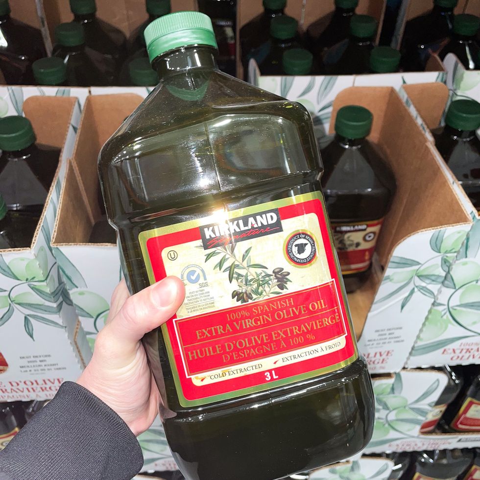 Une main tenant une bouteille de 3 L d'huile d'olive extravierge d'Espagne, au Costco.