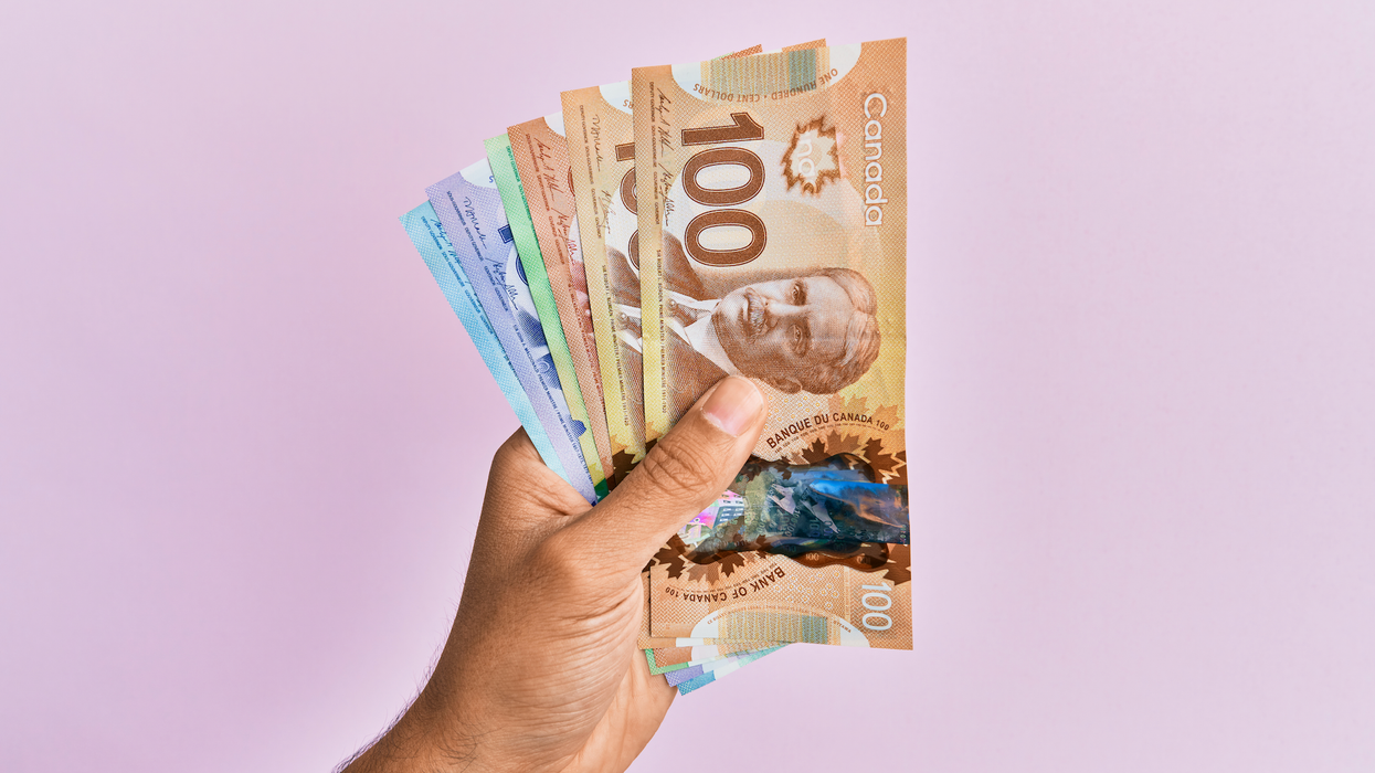 Une main tient des billets d'argent placés en éventail devant un mur mauve.