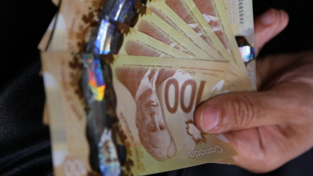 Une main tient des billets de 100 $ en éventail.