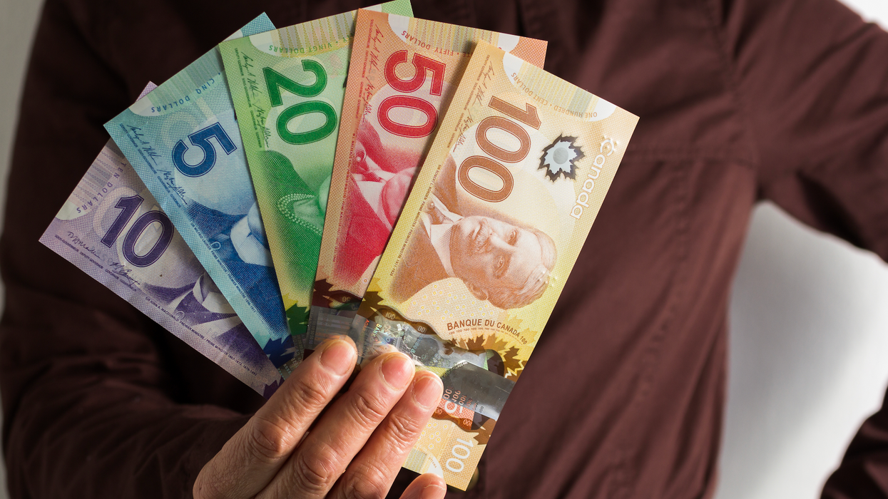 Une main tient des billets de 5 $, 10 $, 20 $, 50 $ et 100 $ en éventail dans sa main.