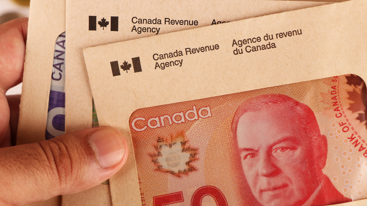 Une main tient des enveloppes de l'Agence du revenu du Canada avec des billets d'argent dedans.
