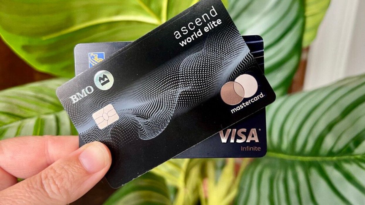 Une main tient deux cartes de crédit Visa et Mastercard noires devant une plante.