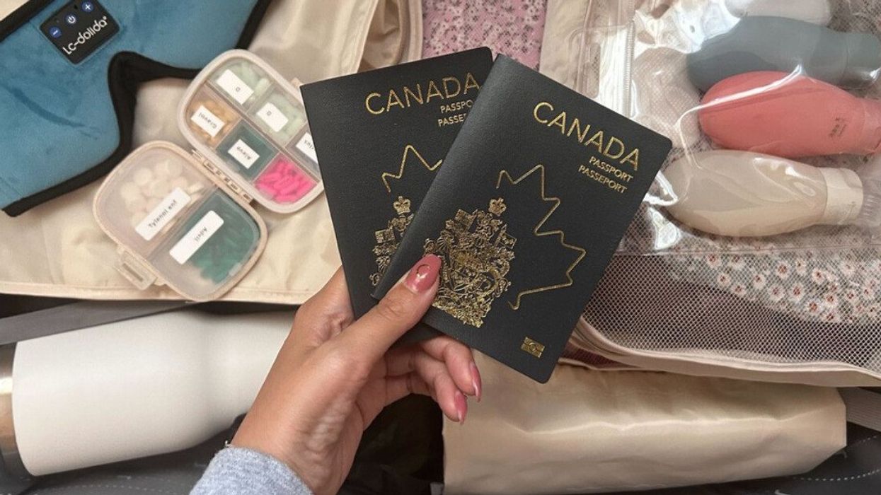 Une main tient deux passeports devant une valise remplie et ouverte.