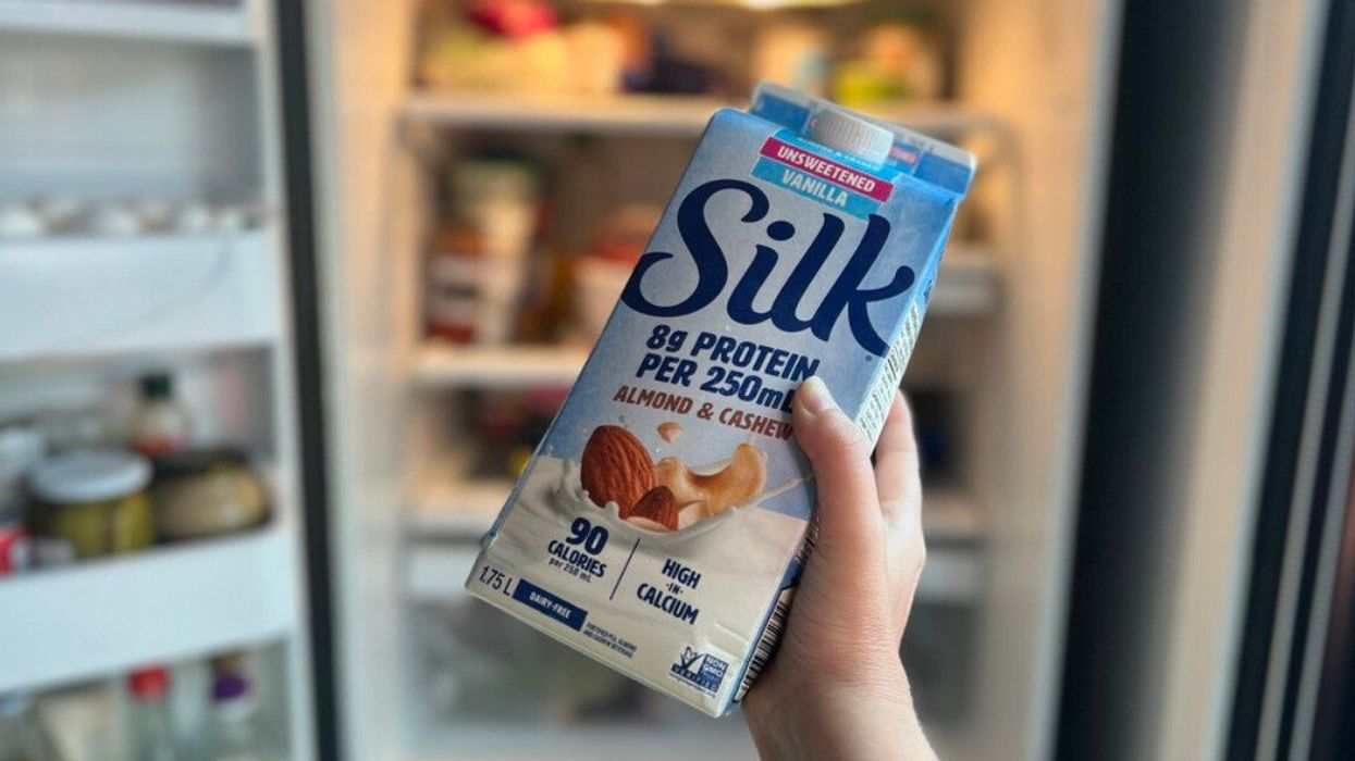 Une main tient un carton de lait végétal devant un frigo ouvert.